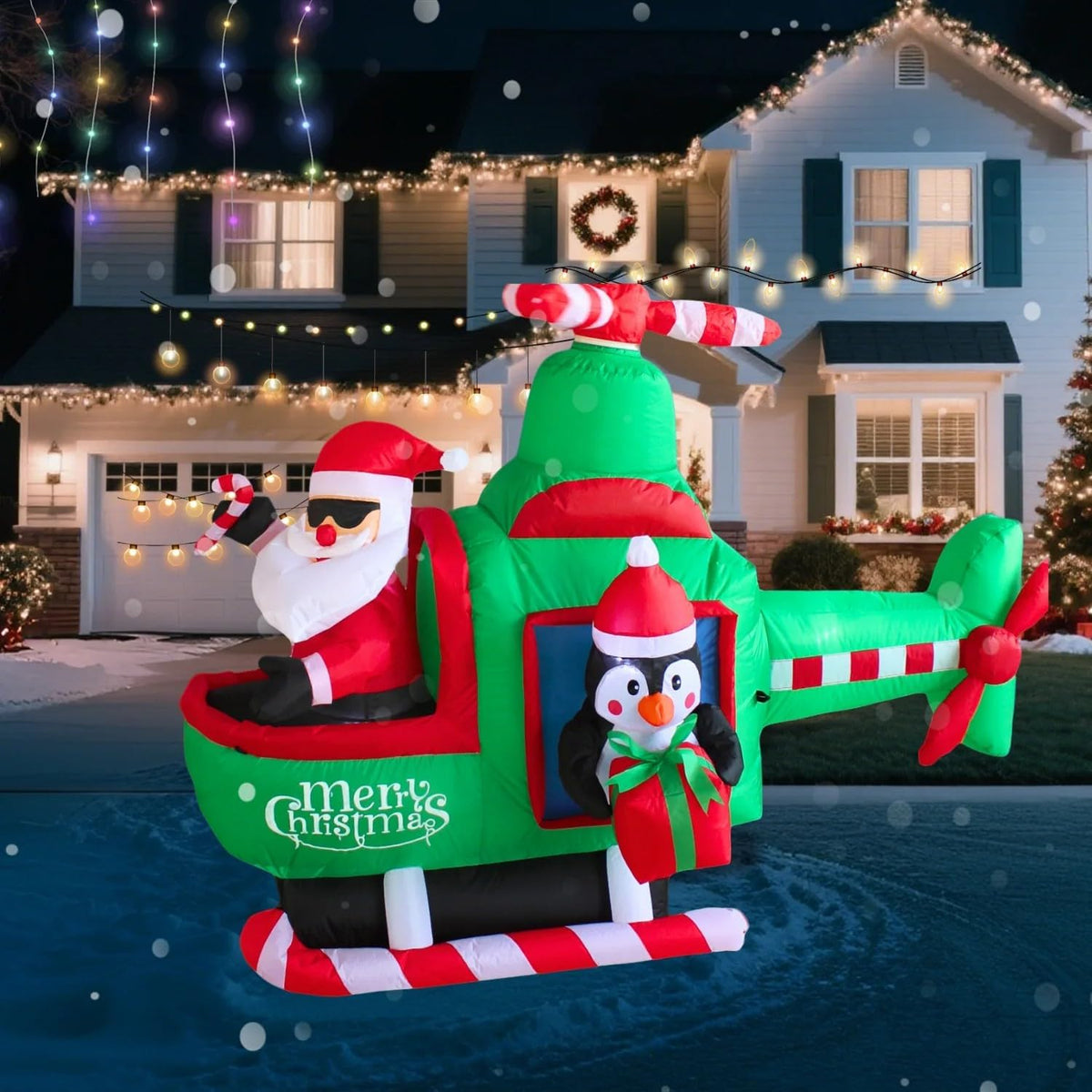 Santa and a penguin in a green and red Merry Christmas helicopter inflatable in a snowy yard