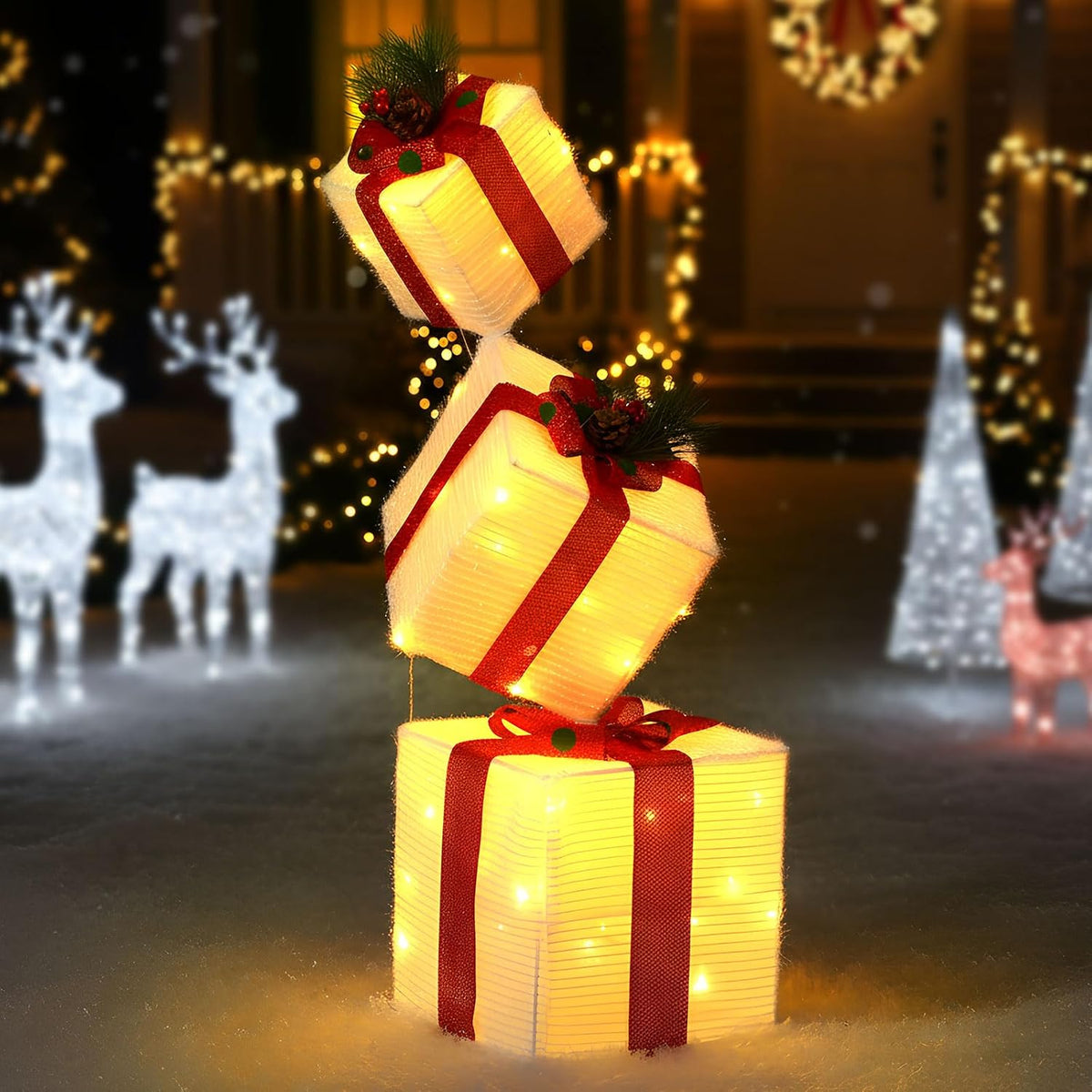 Three lighted cream gift boxes with red ribbons stacked at angles near lit reindeer
