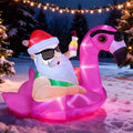Santa in sunglasses lounging on a pink flamingo float inflatable in the snow