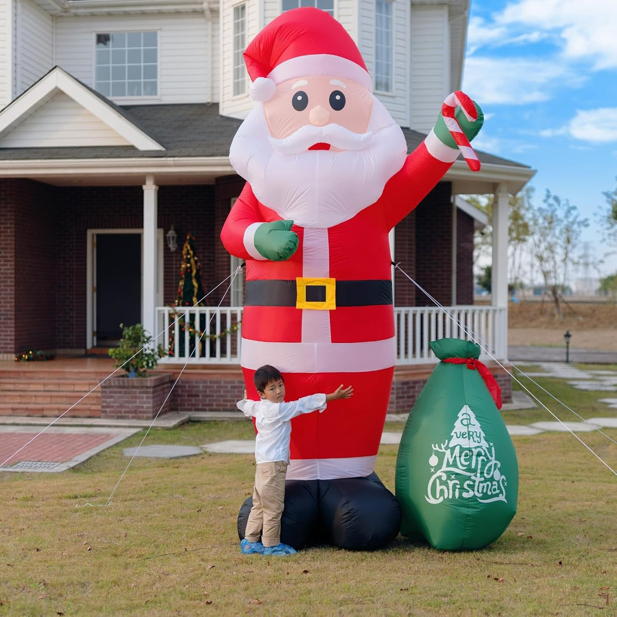Giant Santa inflatable holding a candy cane beside a green gift sack with a child for scale