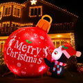 Penguin in a Santa hat beside a glowing red Merry Christmas ornament inflatable in front of a lit house