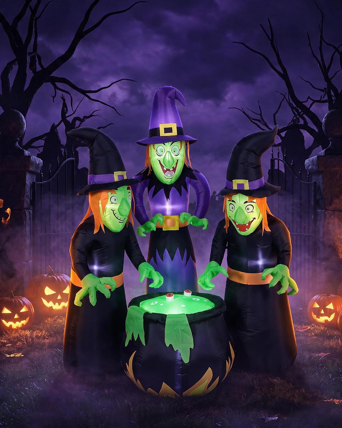 Three green-faced witches around a glowing green cauldron inflatable in a dark yard