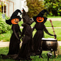 Three witch stakes with glowing jack-o'-lantern heads in black robes around a cauldron on a lawn