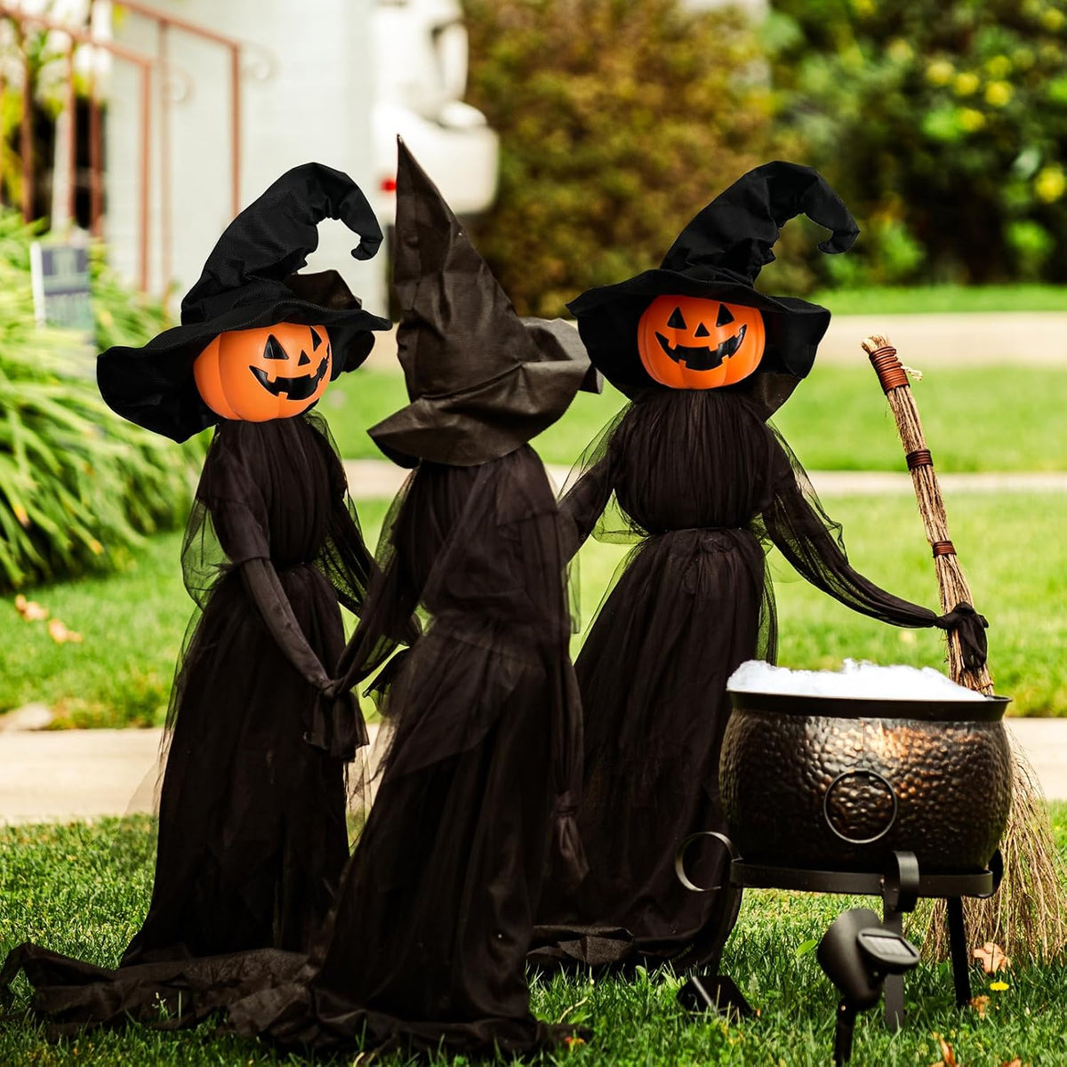 Three witch stakes with glowing jack-o'-lantern heads in black robes around a cauldron on a lawn